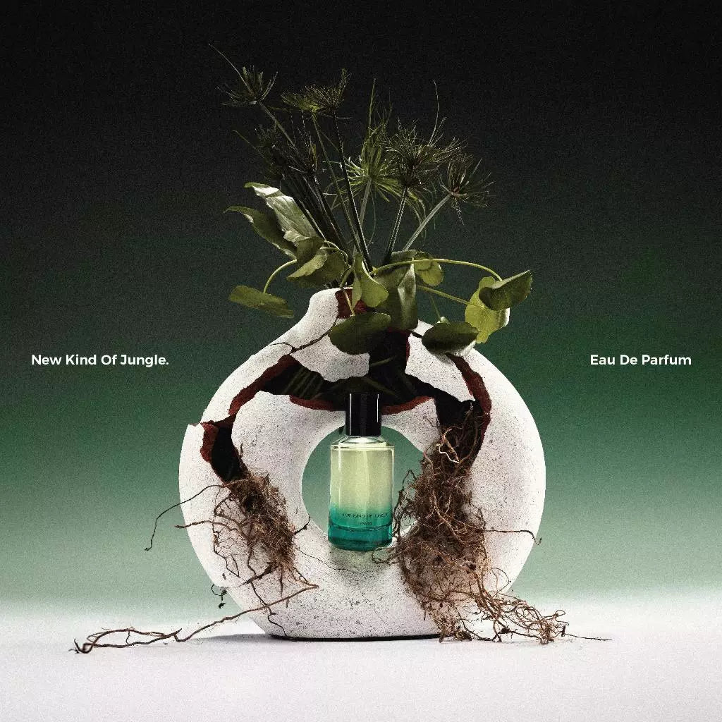 A bottle of 'New Kind Of Jungle' perfume from Scents Of Pluto, placed inside a floral arrangement with greenery and soil, against a dark background.