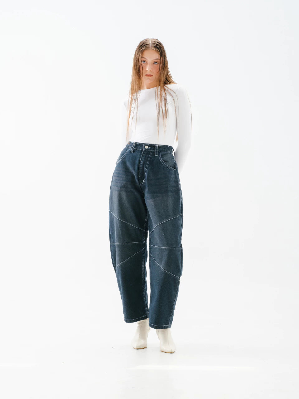 Person wearing blue denim barrel pants and a white top on a white background