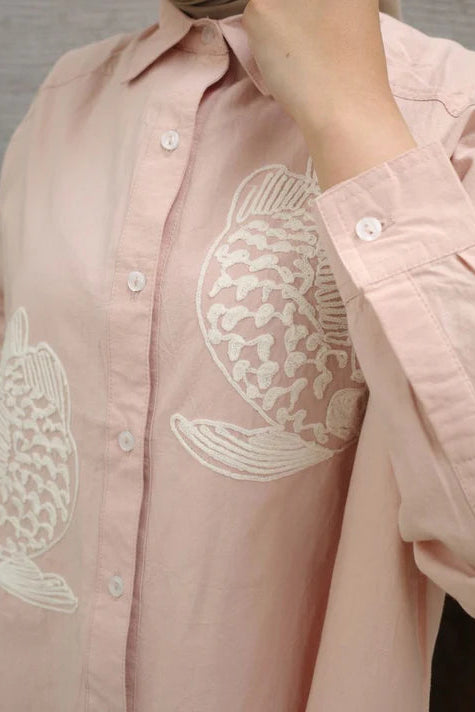 Pink shirt with white fish embroidery by Nona on a plain background