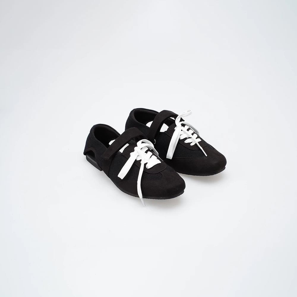 Black flat shoes with white laces on a light gray background