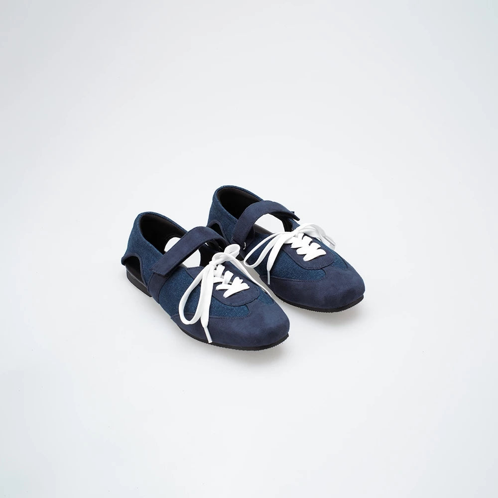 Pair of navy blue flat shoes with white laces on a light gray background