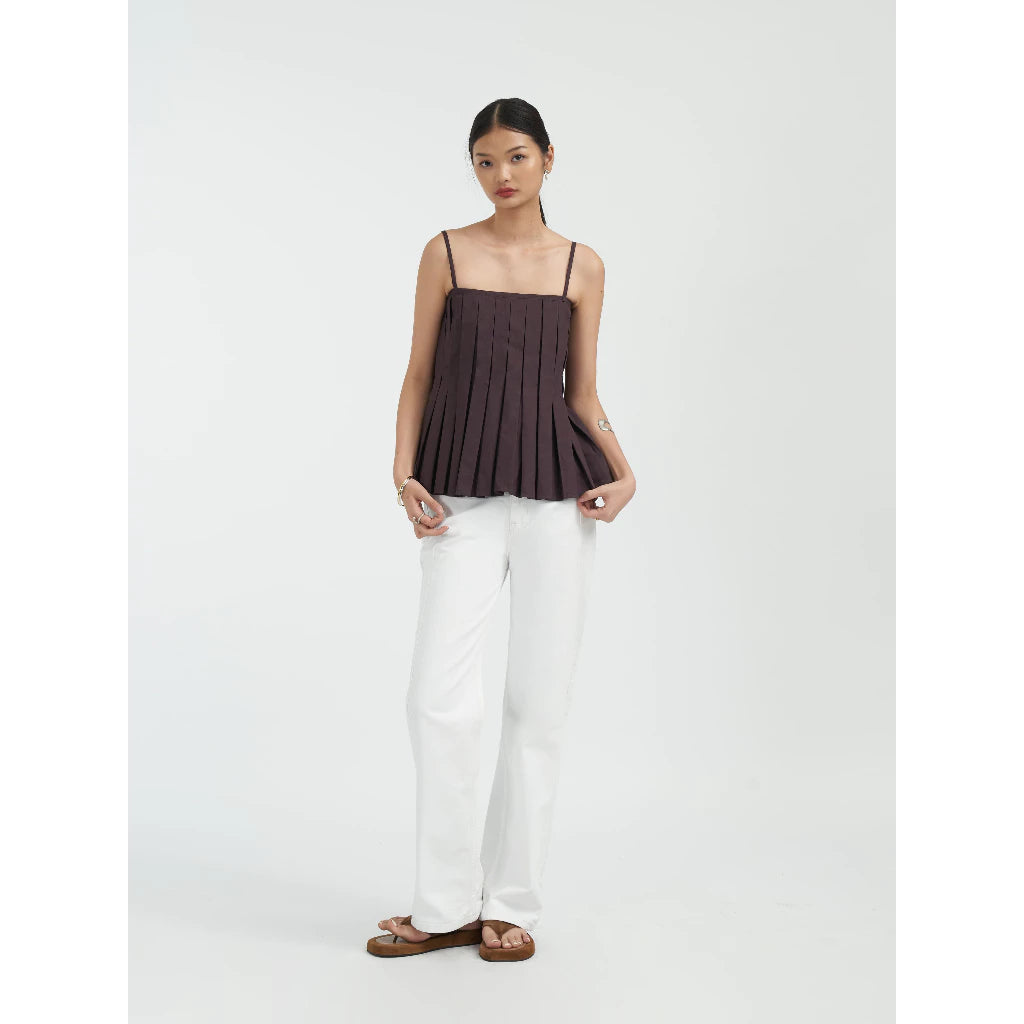 Woman wearing a dark brown pleated top and white jeans by Achete de Nous on a white background