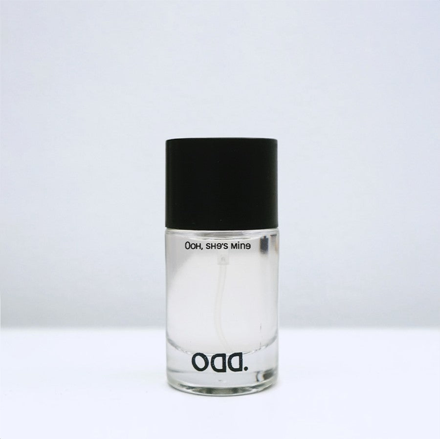 A bottle of 'Ooh She's Mine' perfume by ODD with a black cap and clear label.