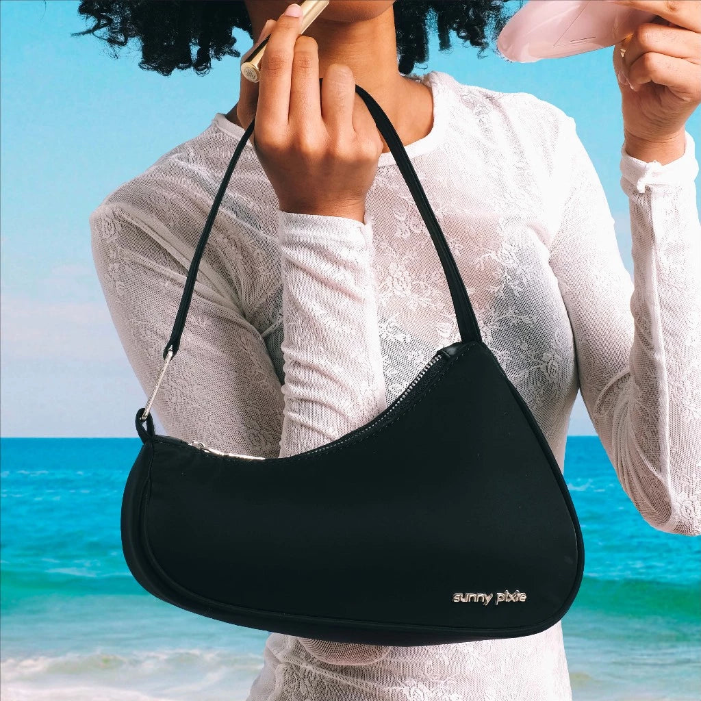 A sleek black women’s shoulder bag with a modern crescent silhouette, featuring a smooth finish and a subtle metal “sunny pixie” logo on the front. The slim strap adds a minimalist touch, making it perfect for everyday wear or casual outings.

Tas wanita hitam dengan siluet crescent yang modern, dilengkapi permukaan yang sleek dan logo metal “sunny pixie” di bagian depan. Tali bahu yang ramping memberi sentuhan minimalis, ideal untuk dipakai sehari-hari maupun saat hangout santai.