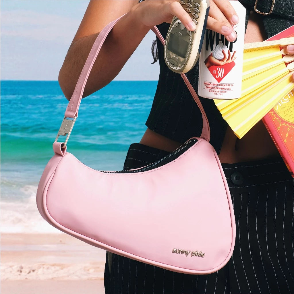 A sleek pink women’s shoulder bag with a modern crescent silhouette, featuring a smooth finish and a subtle metal “sunny pixie” logo on the front. The slim strap adds a minimalist touch, making it perfect for everyday wear or casual outings.

Tas wanita pink dengan siluet crescent yang modern, dilengkapi permukaan yang sleek dan logo metal “sunny pixie” di bagian depan. Tali bahu yang ramping memberi sentuhan minimalis, ideal untuk dipakai sehari-hari maupun saat hangout santai.