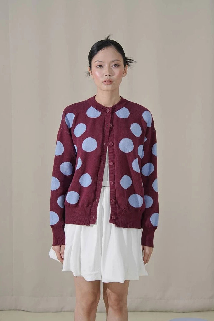 Woman wearing a maroon cardigan with blue polka dots by Tuff Puff against a plain background