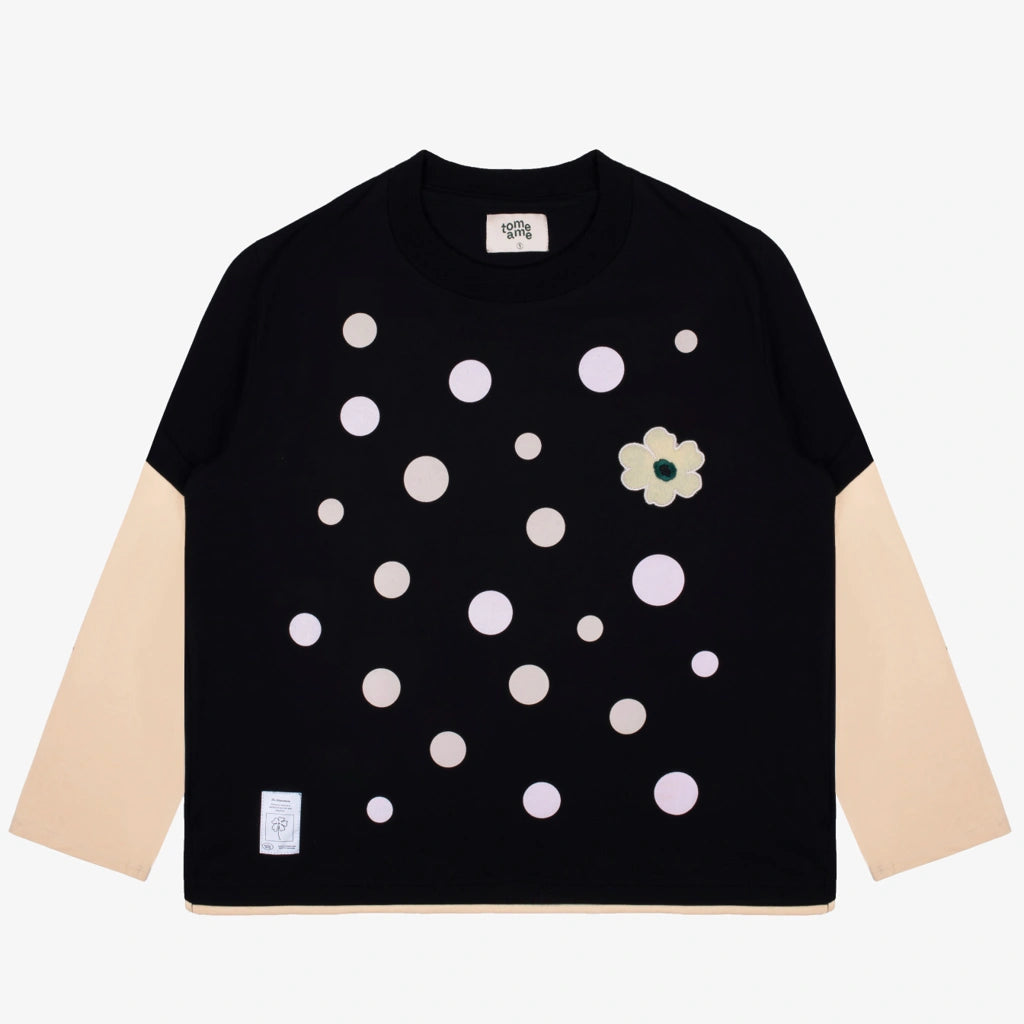Black t-shirt with white polka dots and a flower design from Tome Ame on a light gray background
