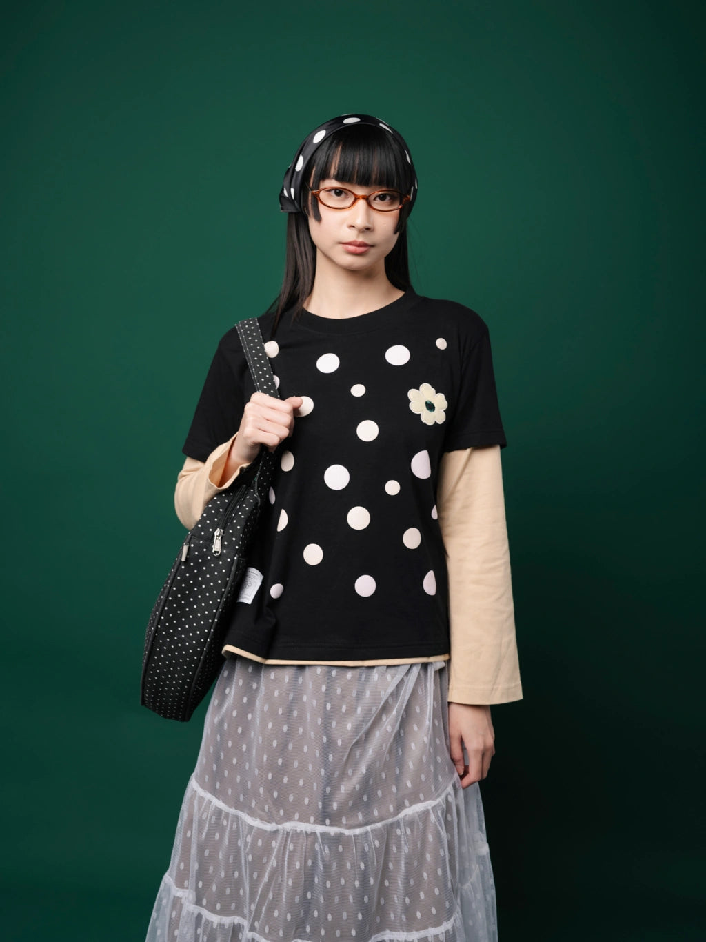 Woman wearing a black polka dot shirt and gray skirt against a green background