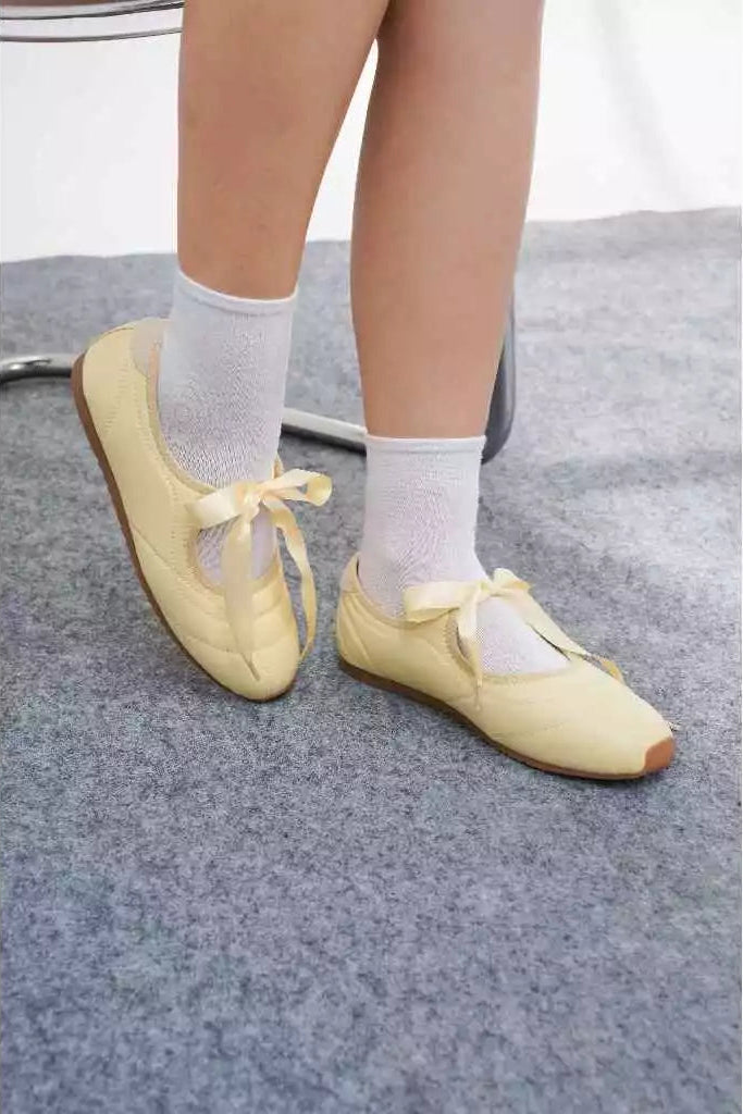 Yellow ballet flatshoes worn with white socks on a gray floor.

Flat shoes wanita berwarna kuning yang dikenakan dengan kaus kaki putih di atas latar lantai abu-abu