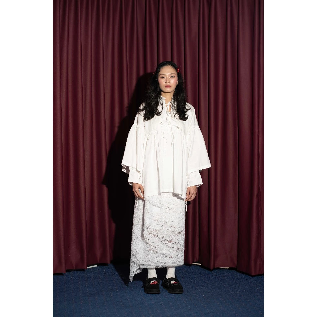 Person wearing a white blouse by Tuff Puff with a patterned skirt against a red curtain.