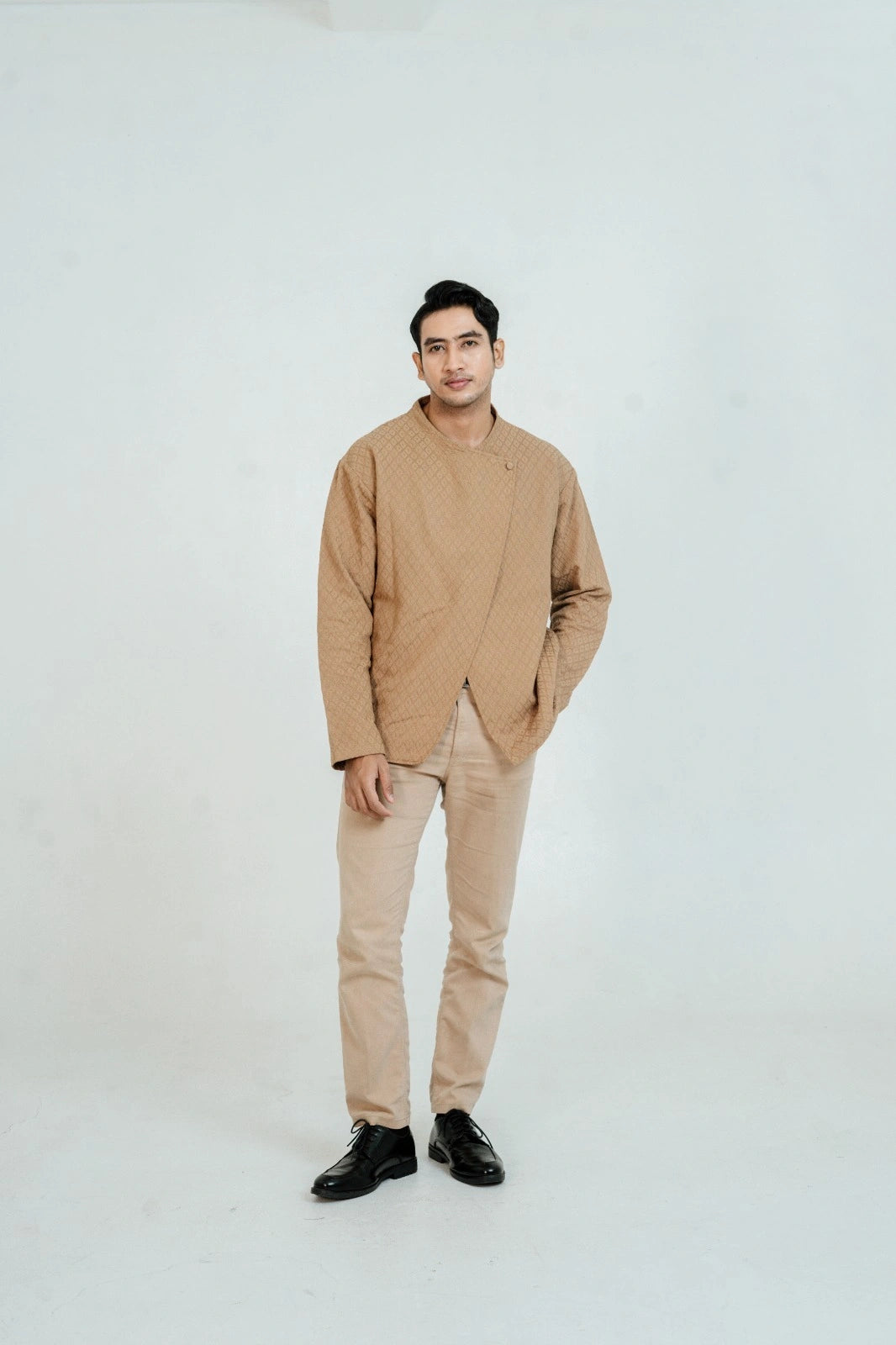 Man wearing a brown beskap by Damakara with a beige pants on a white background