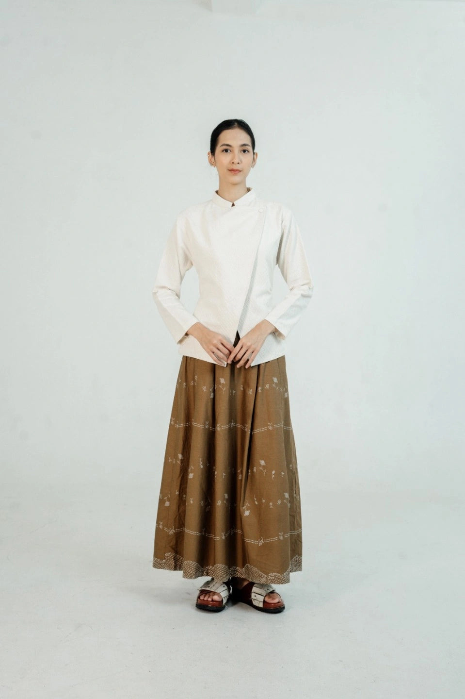 Person wearing a white suit by Damakara and brown patterned skirt on a plain background