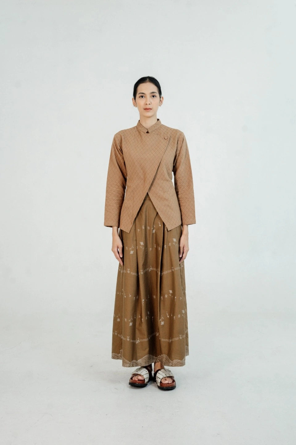 Woman wearing a brown suit by Damakara with a patterned skirt on a white background