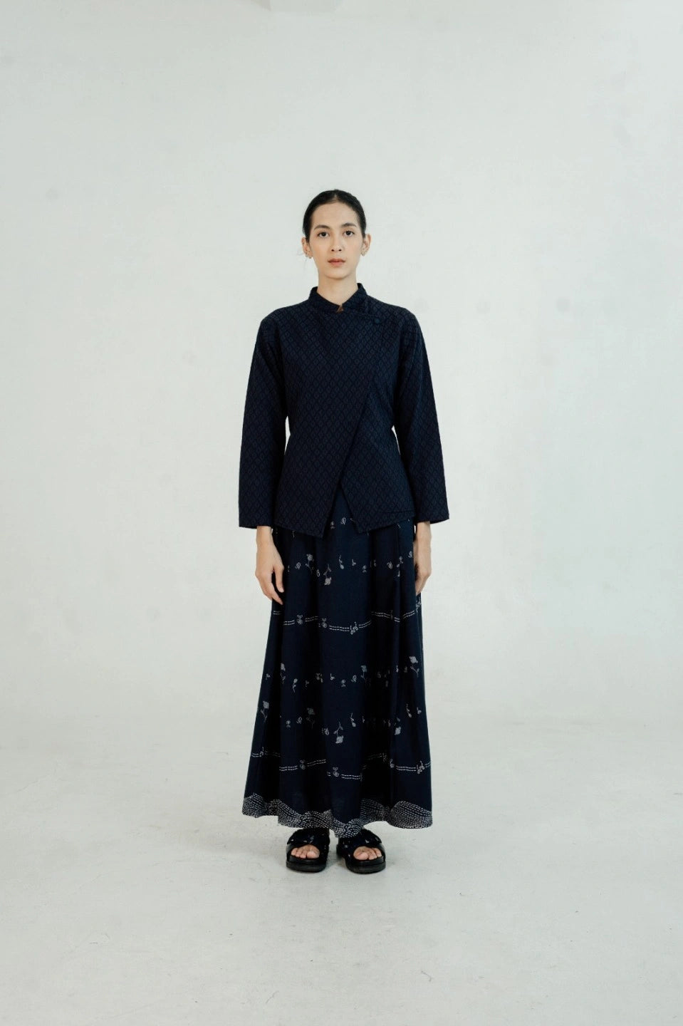Person wearing a navy suit by Damakara with a patterned skirt on a white background