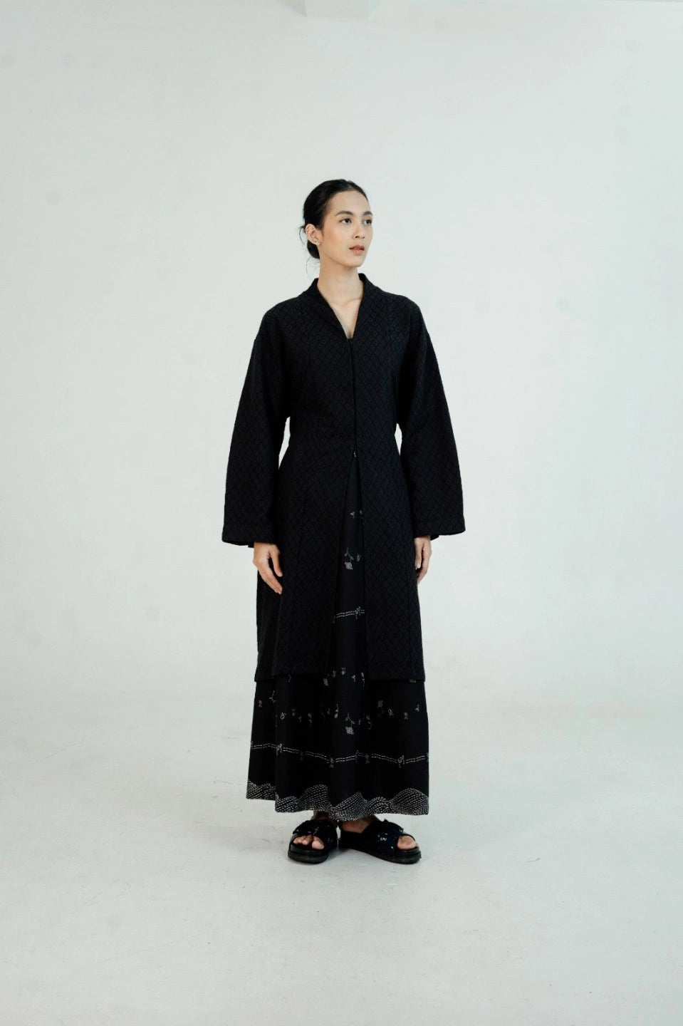 Person wearing a black long tunic by Damakara on a white background