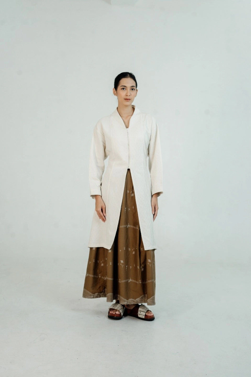 Person wearing a long white tunic by Damakara over a brown dress on a white background