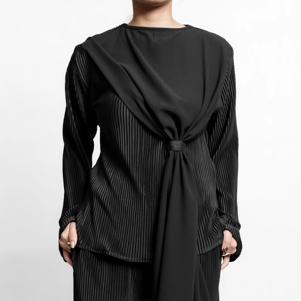 Black pleated top with long sleeves by Isoos Studios on a plain background