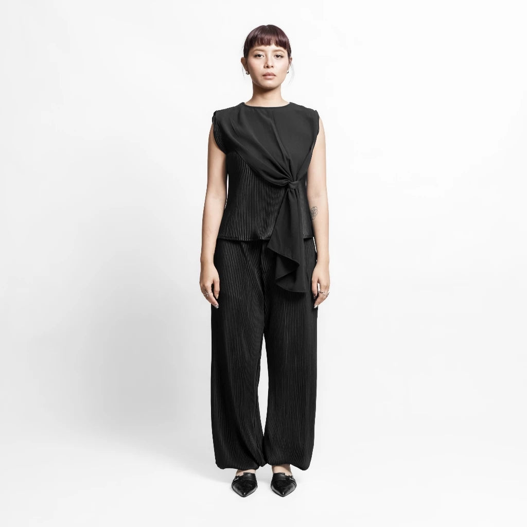 Person wearing a black outfit by Isoos Studios with a tied top on a white background