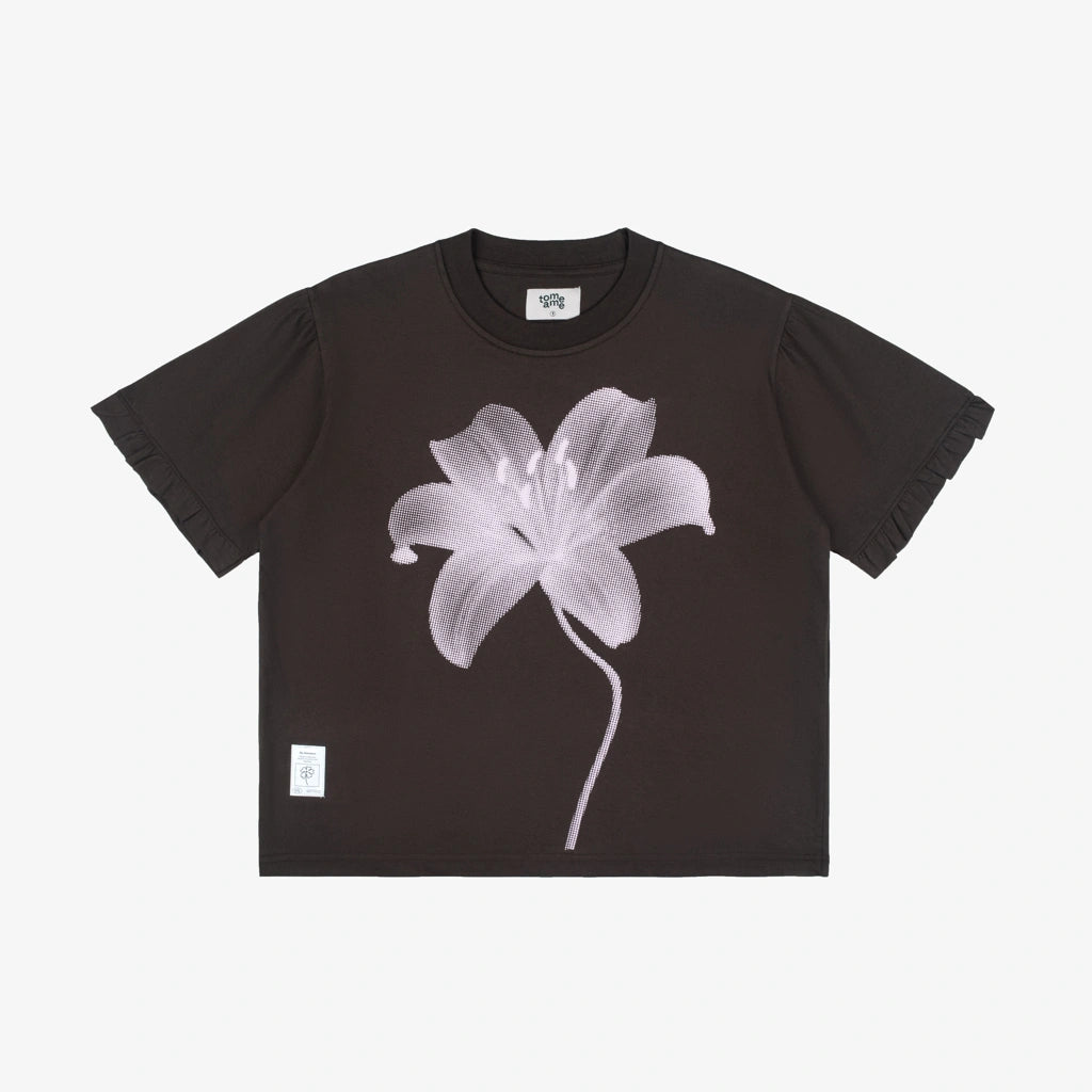 A dark brown short-sleeve crop top t-shirt by Tome Ame featuring a large white and light gray lily flower graphic on the front, displayed flat against a light gray background.