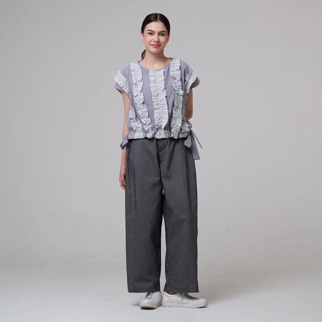 Woman wearing Reta Vest, a gray ruffled top from Aumone, paired with wide-leg pants on a plain background.