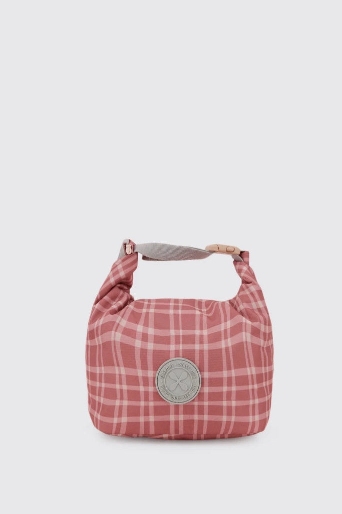 A pink and white plaid canvas lunch bag by Exsport Bag with a top handle and a circular silver-tone metal logo plate on the front, set against a solid light gray background.