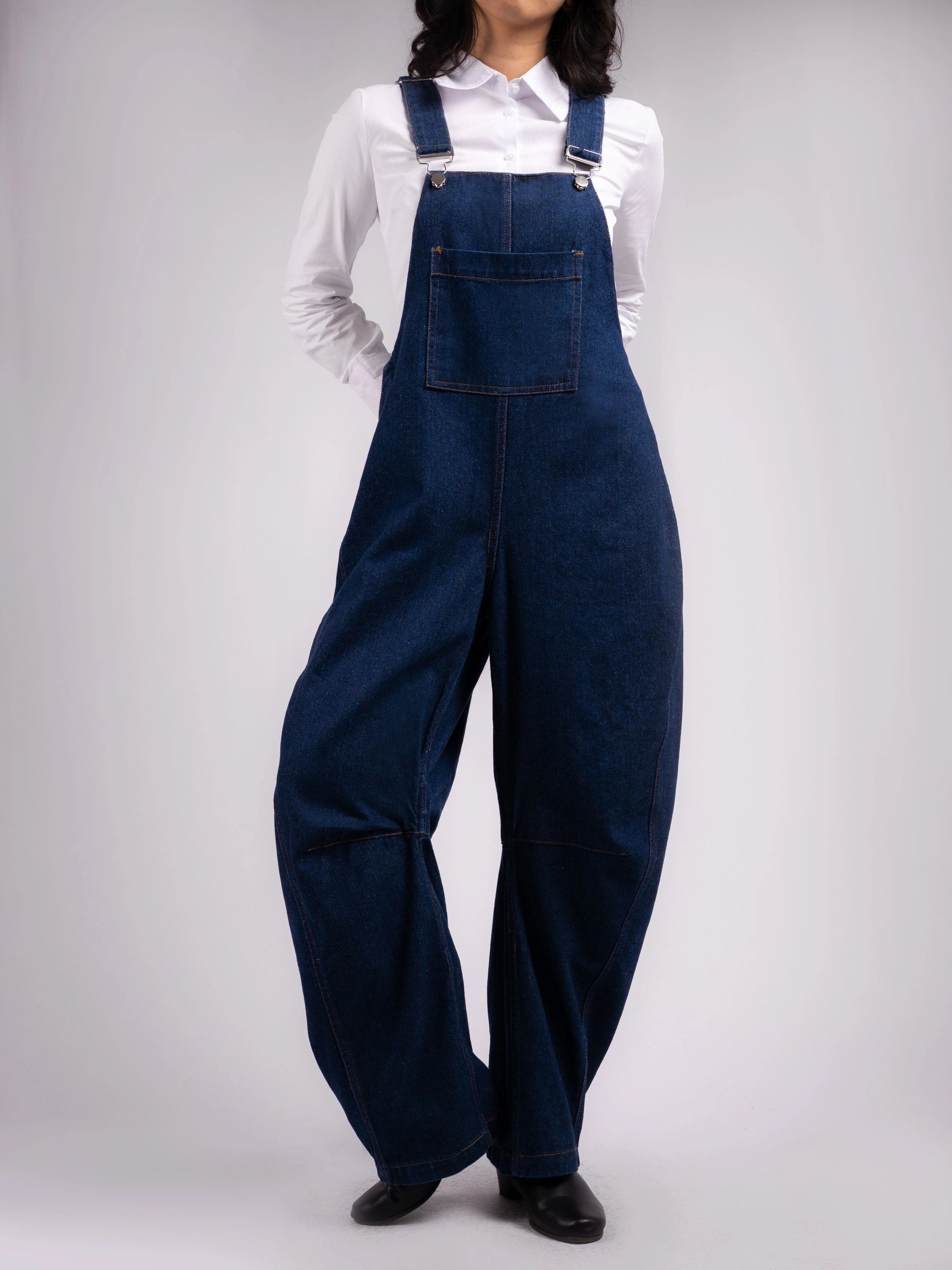 Person wearing blue denim barrel overalls on a white background