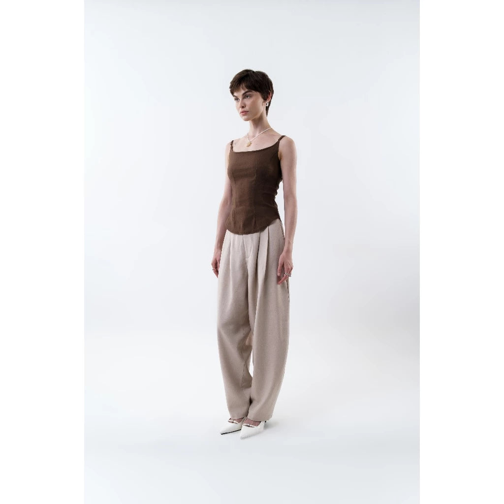 Woman wearing a brown tank top by Morningsol and beige pants on a white background