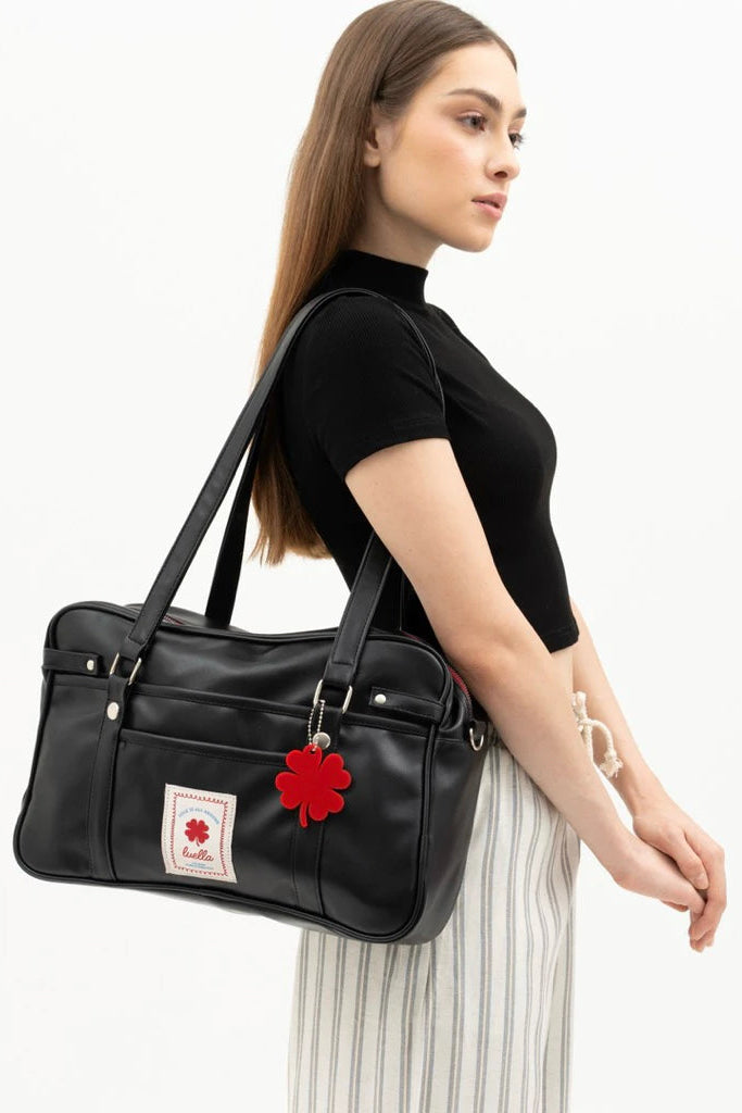 Woman carrying a black tote bag by Luella with a red flower emblem on a white background