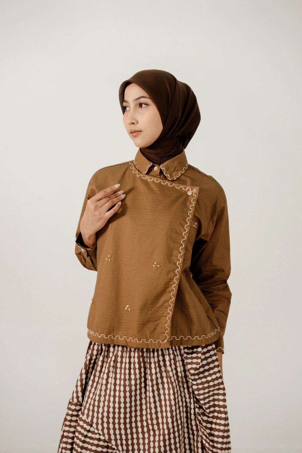 Woman wearing a brown top by Damakara with embroidery and a checkered skirt on a white background