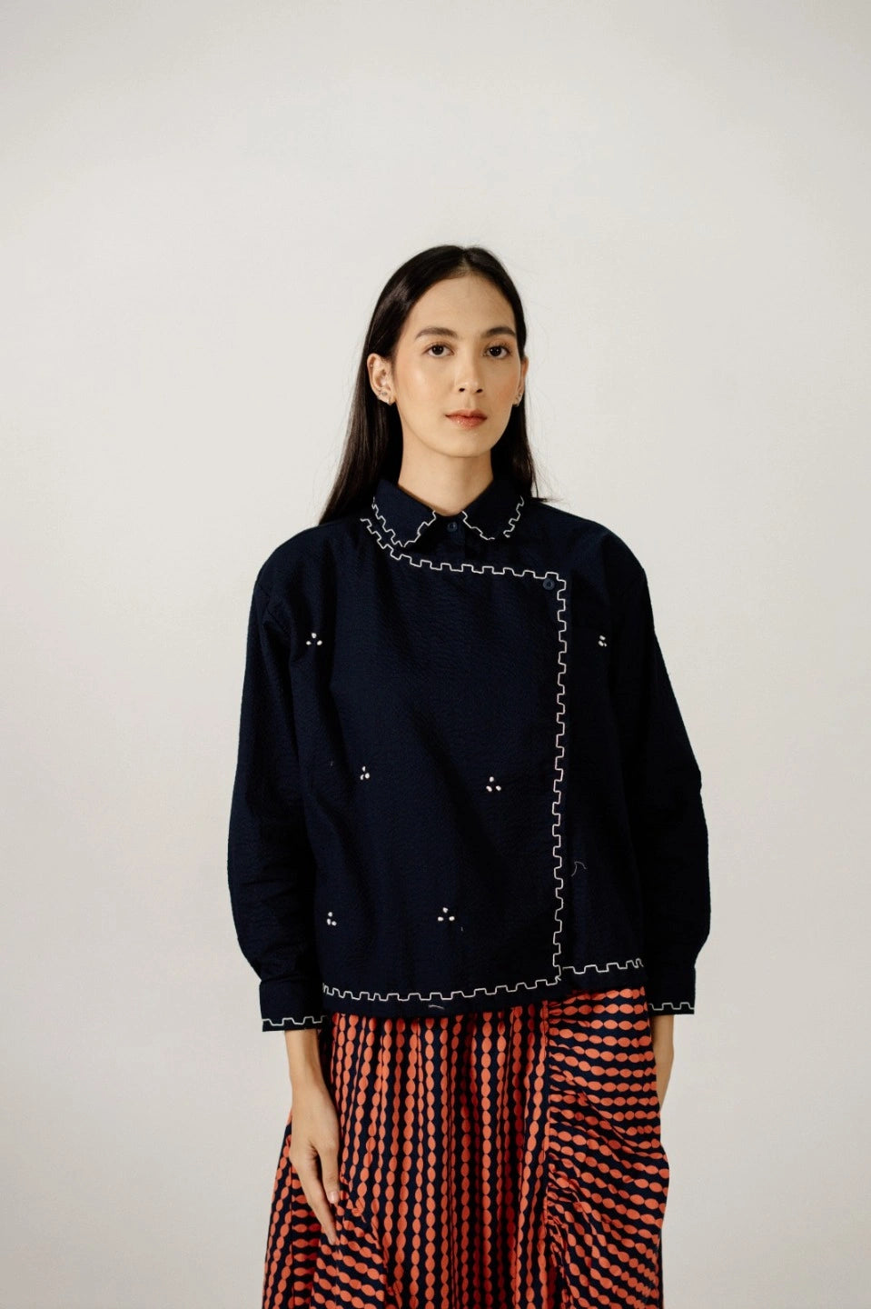 Woman wearing a dark blue top by Damakara with intricate detailing and a red and black checkered skirt on a plain background