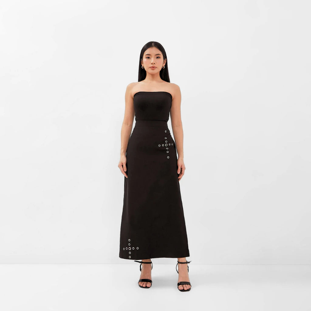 Woman wearing a black strapless top and black skirt with button details on a white background