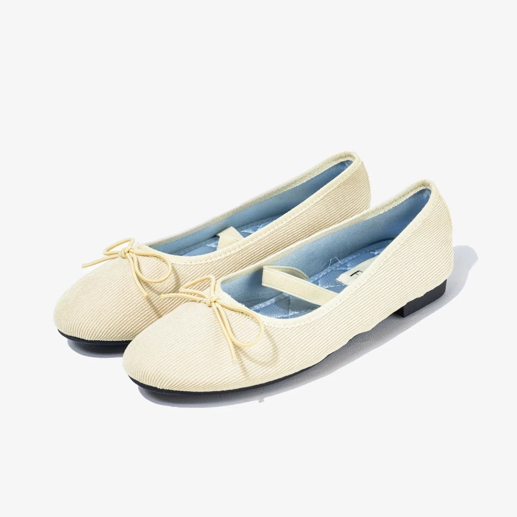 Pair of cream-colored ballet flatshoes with a bow accents on a white background