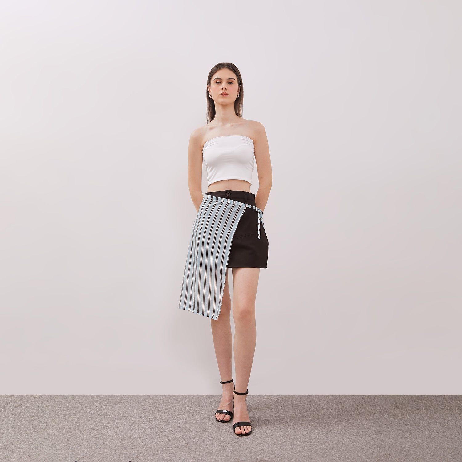 Woman wearing a white strapless top and black and white striped layered mini skirt against a plain background