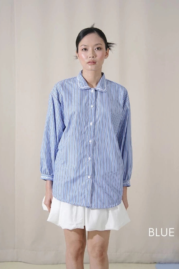Person wearing a blue striped shirt by Tuff Puff and white skirt against a plain background