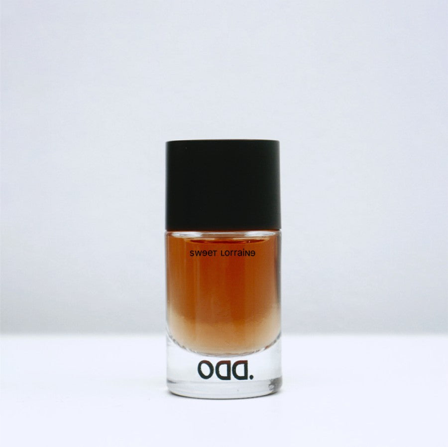 A bottle of fragrance named 'Sweet Lorraine' from the brand ODD, with a dark cap and a clear, amber-colored liquid visible through the bottle.