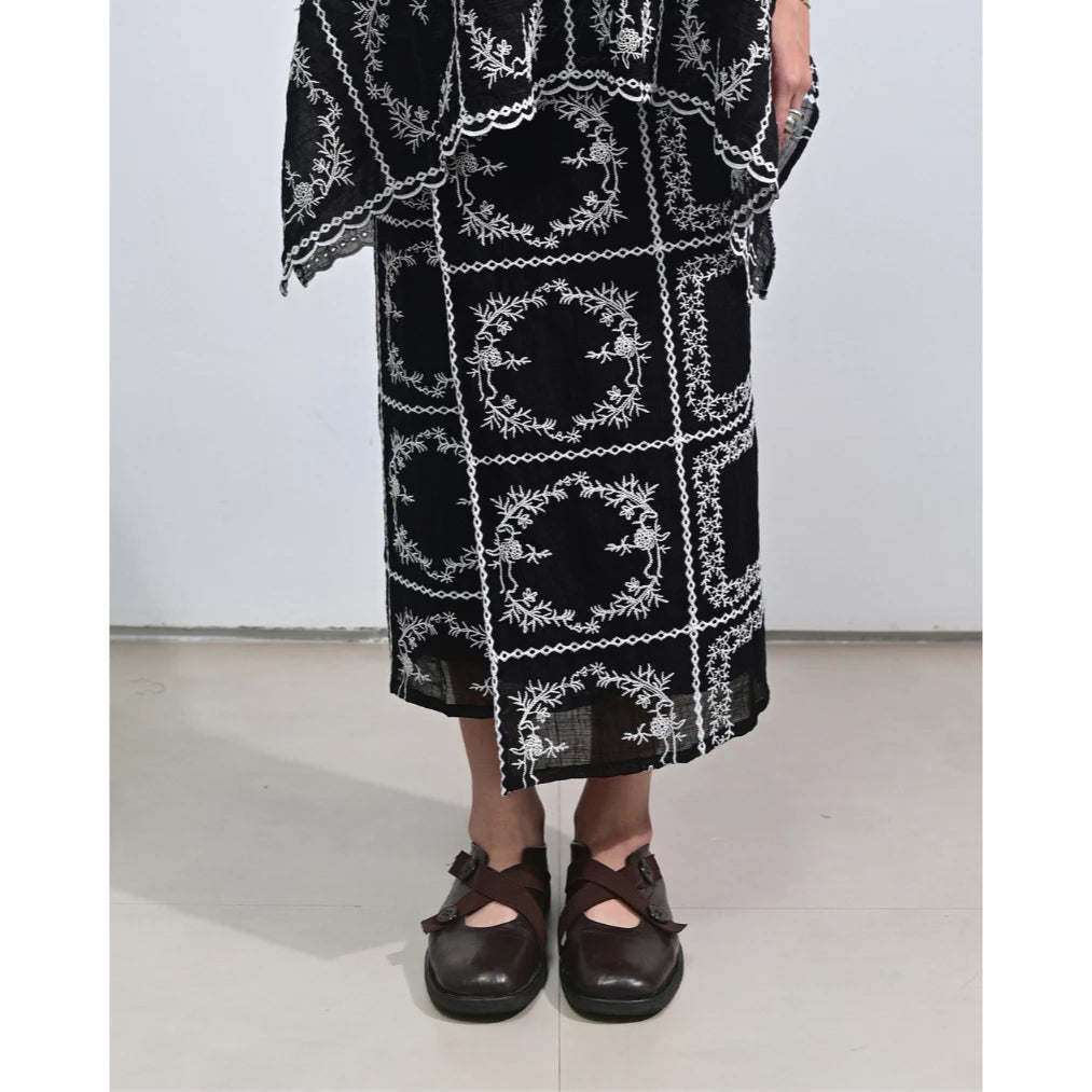 Person wearing a black skirt by Tuff Puff with white embroidery on a plain background