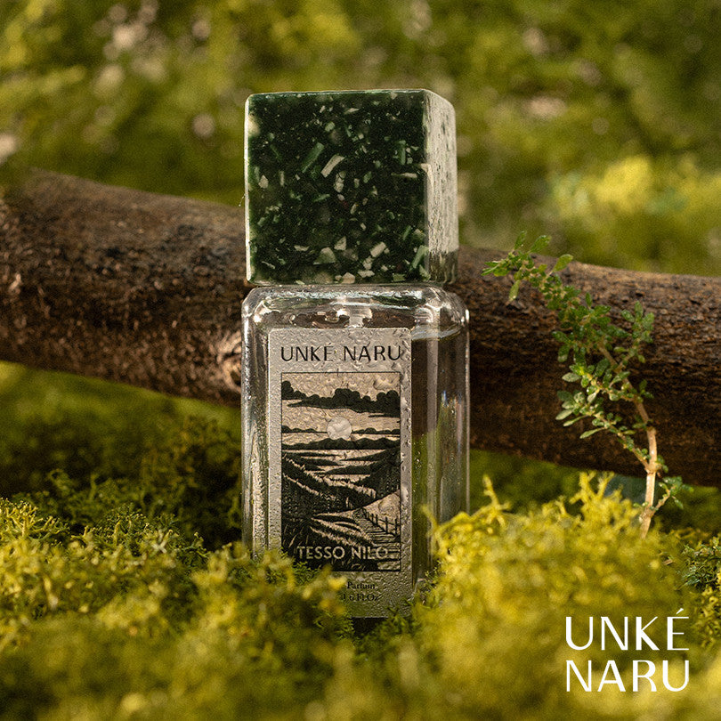 A bottle of Tesso Nilo perfume by Unke Naru placed on a mossy ground with a tree in the background.
