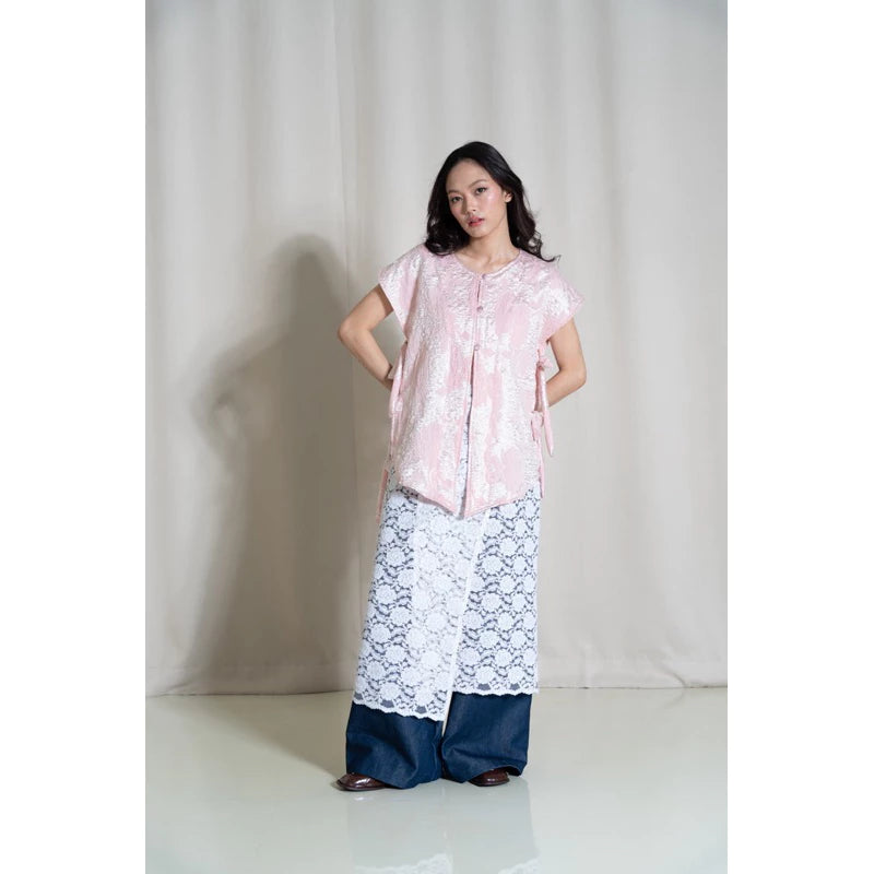 A person wearing a traditional jacquard woven vest in pink floral patterns, named Vas Bunga Vest from Tuff Puff, paired with blue trousers.