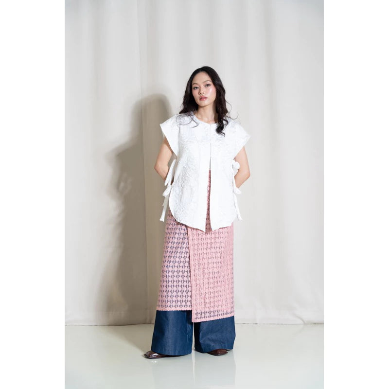 A person wearing a traditional jacquard woven vest in white floral patterns, named Vas Bunga Vest from Tuff Puff, paired with blue trousers.