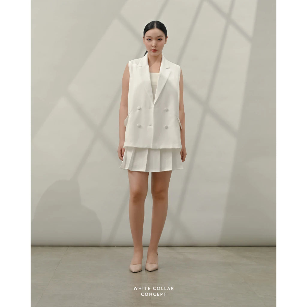 Woman wearing a white vest and skirt set against a neutral background