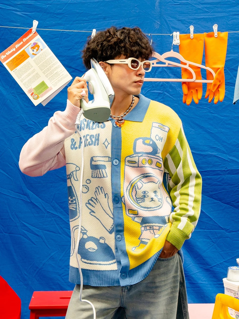 Person wearing a colorful knitted cardigan with cartoon designs by Oh.Irv against a blue background