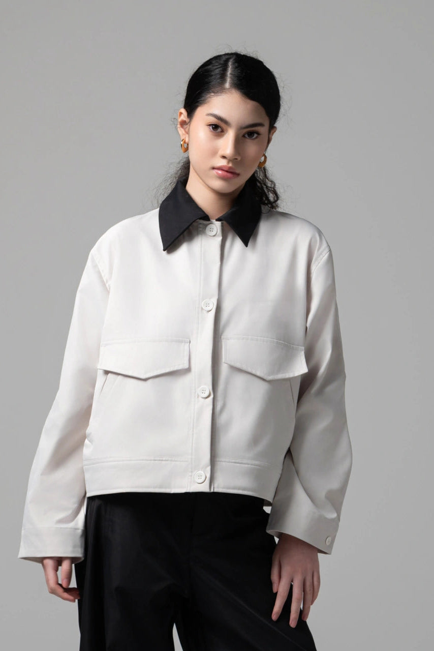 Person wearing a broken white trucker jacket with black collar and cuffs by Kajuaruna on a gray background