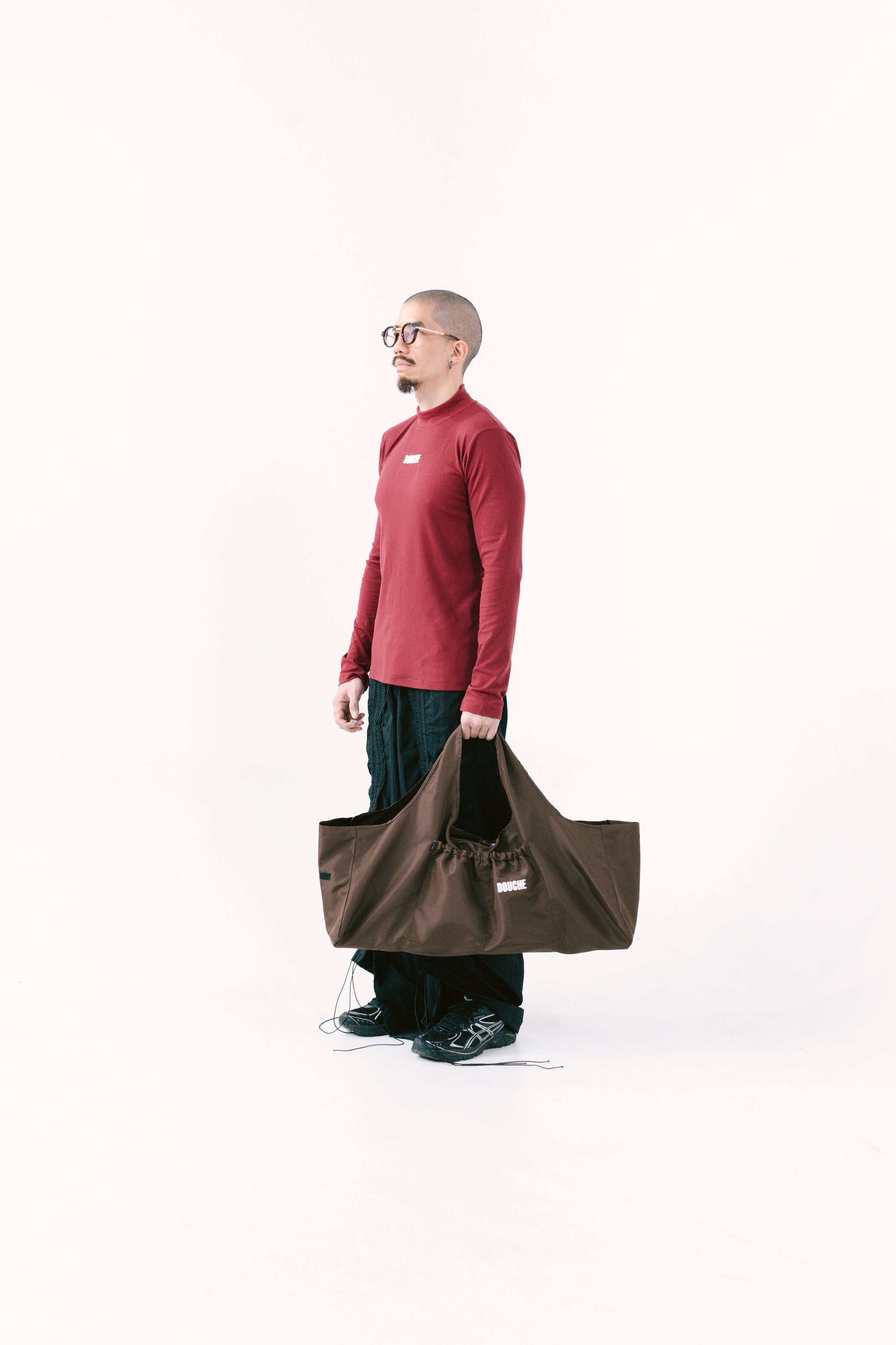 Person holding a dark brown yoga mat bag against a white background