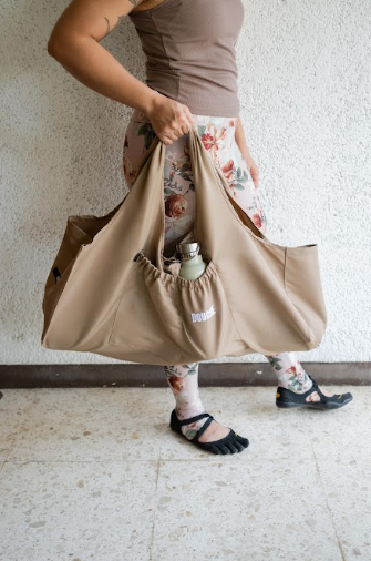 Person holding a light brown yoga mat bag with a neutral background