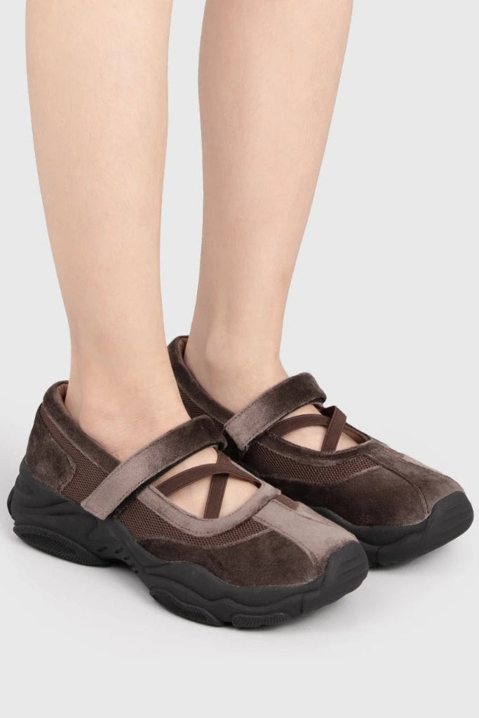 Brown ballerina shoes by Adorable Projects with black soles worn by a person on a light gray background